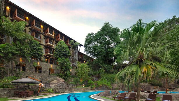 Un hotel con piscina, sillas de descanso y un jardín exuberante.