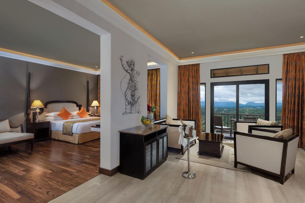 Una habitación de hotel moderna con cama, una zona de estar, un ventanal con vistas y un elemento decorativo en la pared.