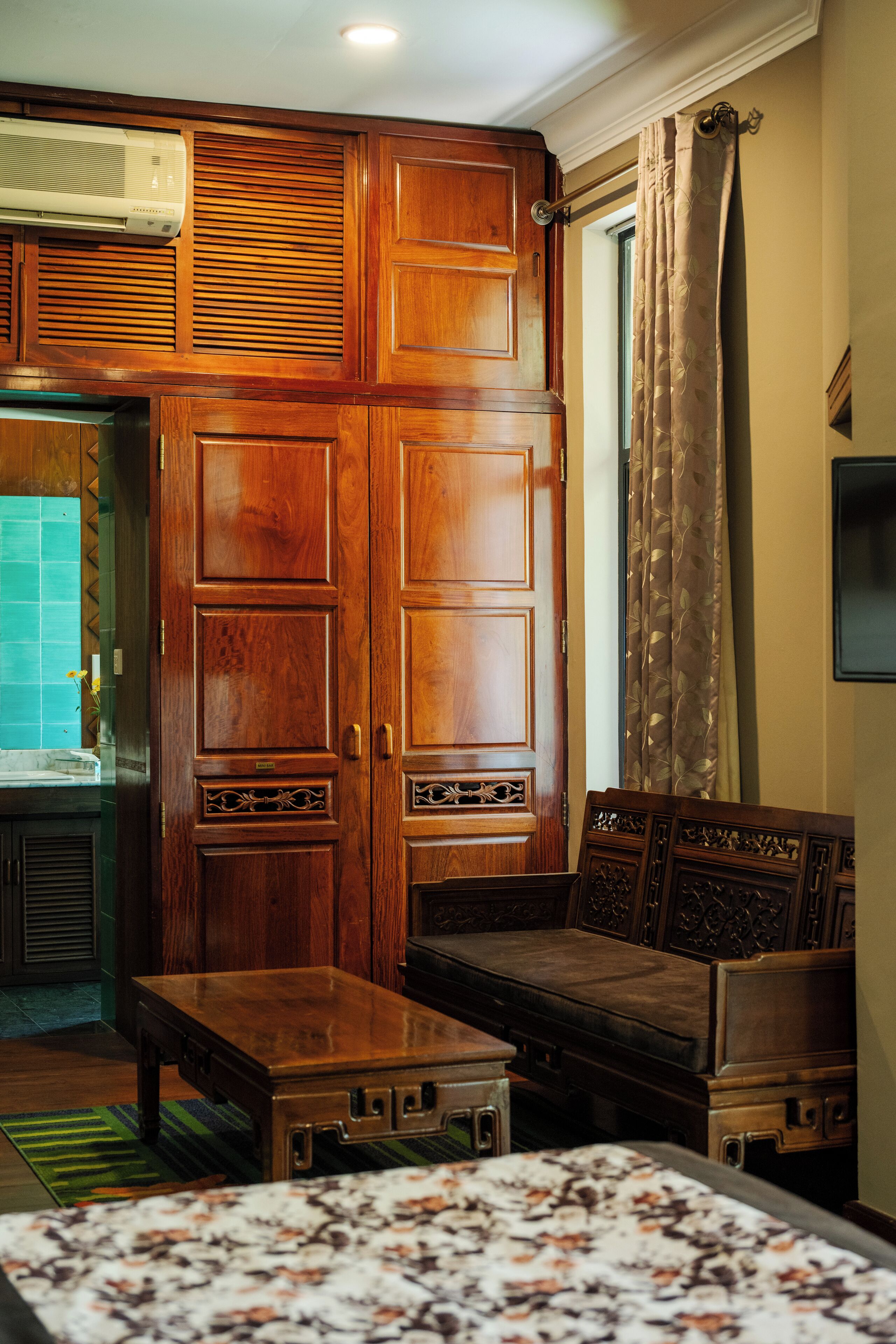 A room with a large wooden wardrobe, a sofa, a small table, and a bed with a floral bedspread.