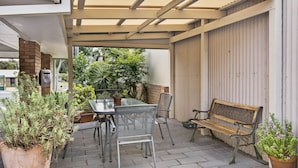 Un patio al aire libre con una mesa, sillas, un banco de madera y plantas en macetas.
