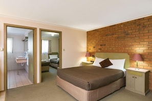 A hotel room with a bed, nightstands, a brick accent wall, and a bathroom visible through an open door. - Bendigo Golden Square Motor Inn (Golden Square)