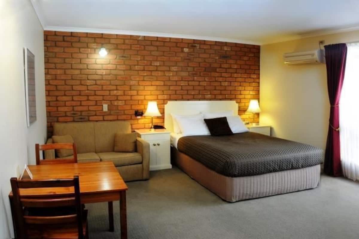 A room with a bed, a wooden table, a sofa, and a brick wall.