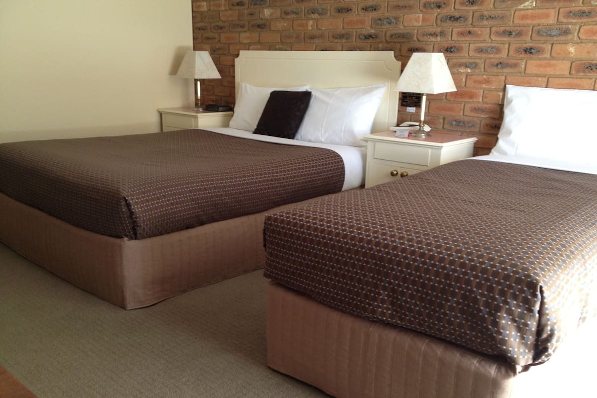 Two twin beds with brown bedding, a brick wall, and a white headboard.
