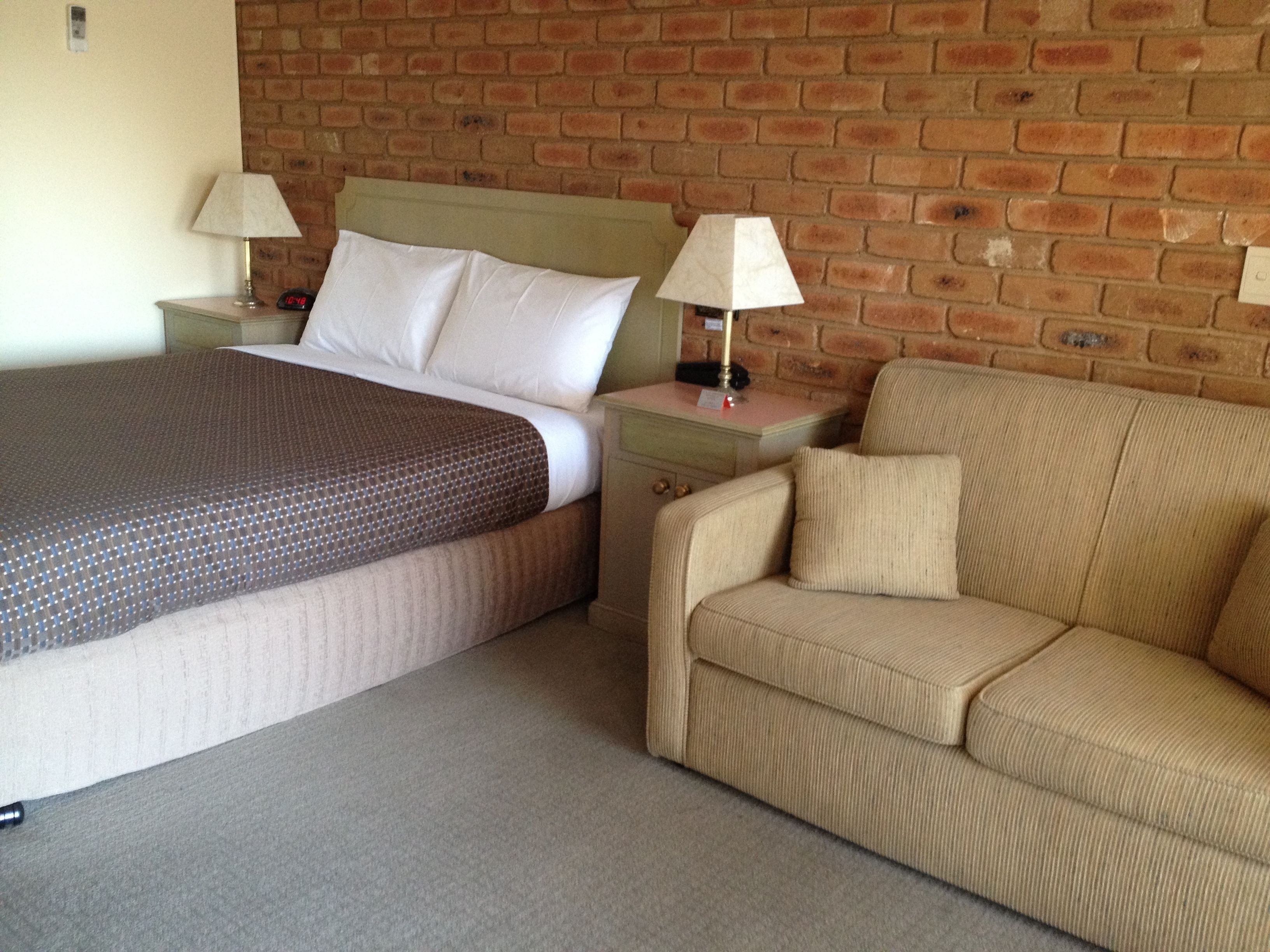 A hotel room with a bed, a nightstand, a lamp, and a sofa.