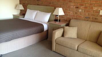 A hotel room with a bed, a nightstand, a lamp, and a sofa.