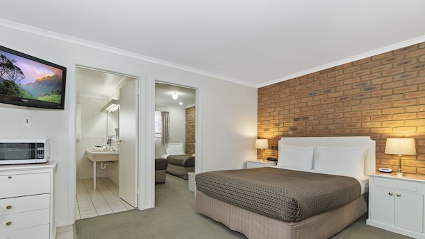 Un dormitorio con cama, mesitas de noche, televisor, microondas y baño visible a través de una puerta abierta.