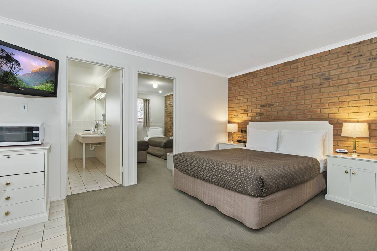 A bedroom with a bed, bedside tables, a TV, a microwave, and a bathroom visible through an open door.