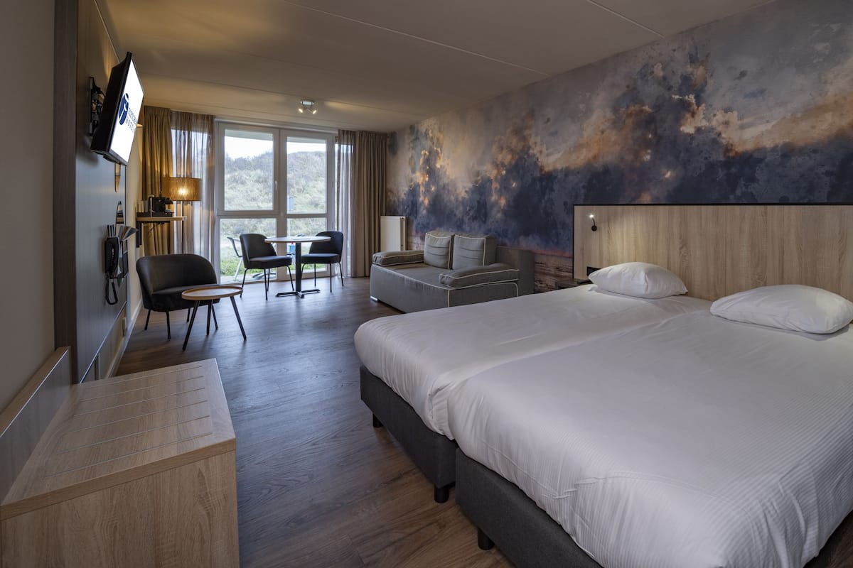 A hotel room with a large bed, a desk, a chair, and a view of the outdoors.