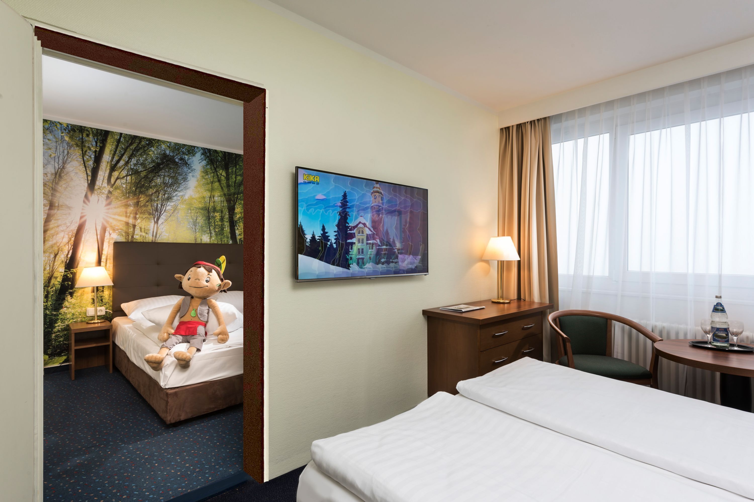 A hotel room with a bed, a nightstand with a lamp, a chair, a desk with a lamp, and a painting on the wall.