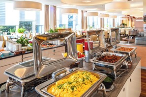 A buffet with various food options, including a large tray of scrambled eggs and a tray of bacon.