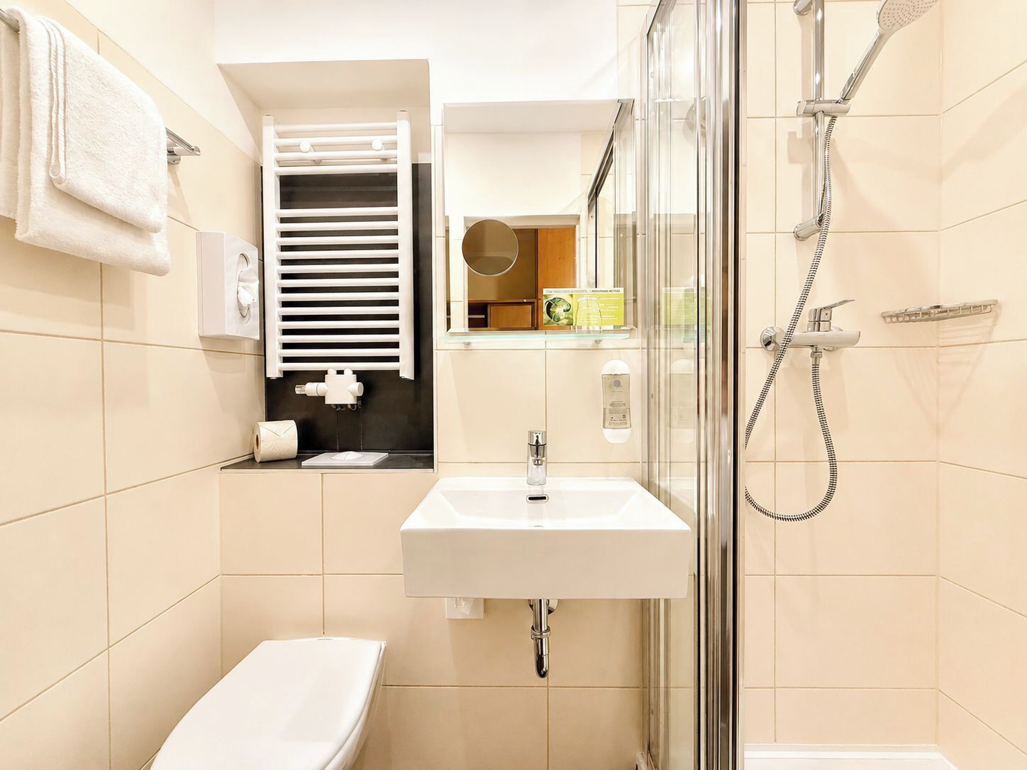 Un baño con inodoro, lavabo, ducha y perchero para toallas.
