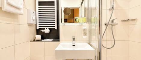 Un baño con inodoro, lavabo, ducha y perchero para toallas.