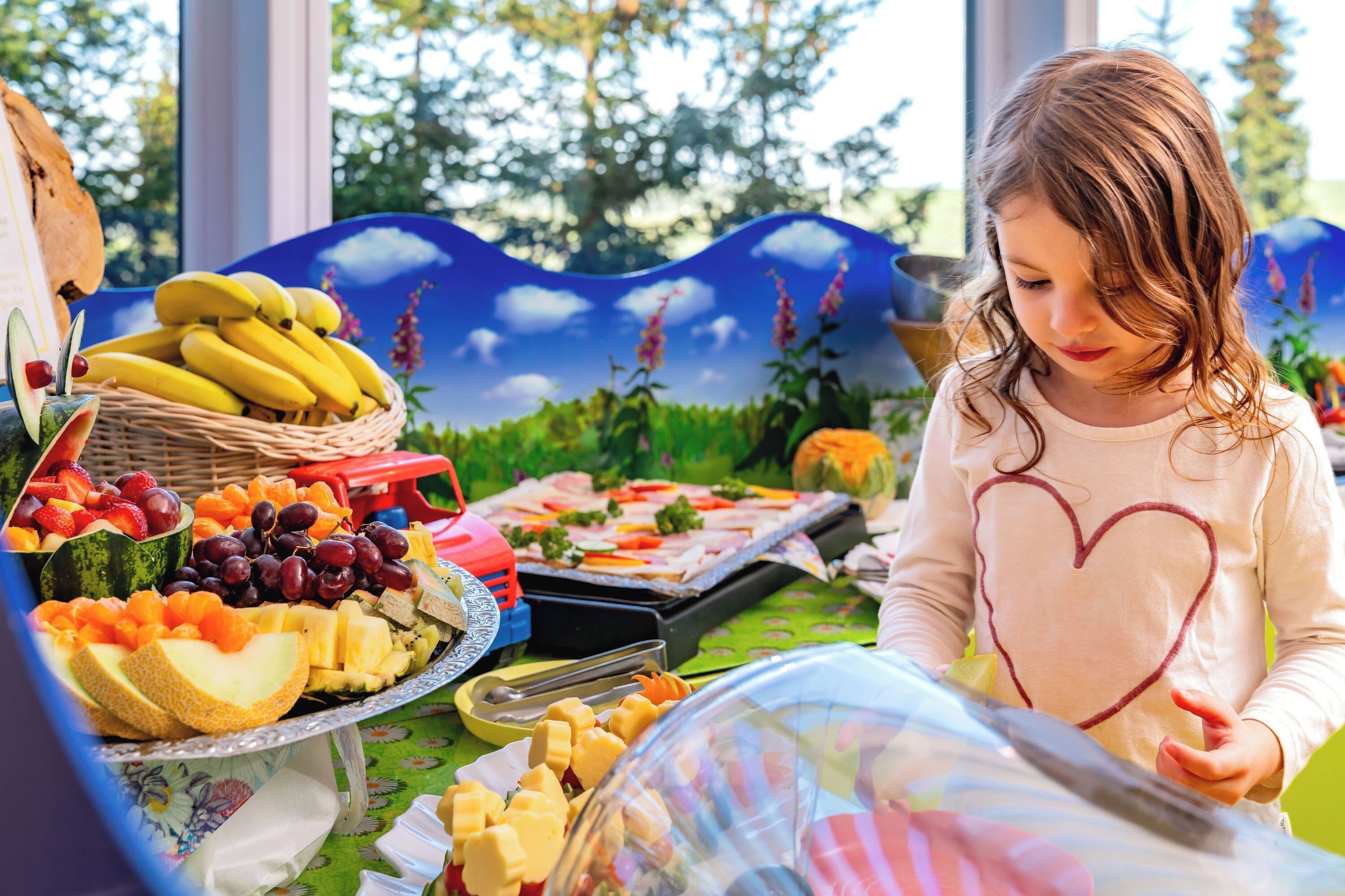 Une table garnie de divers fruits, avec un enfant assis devant.