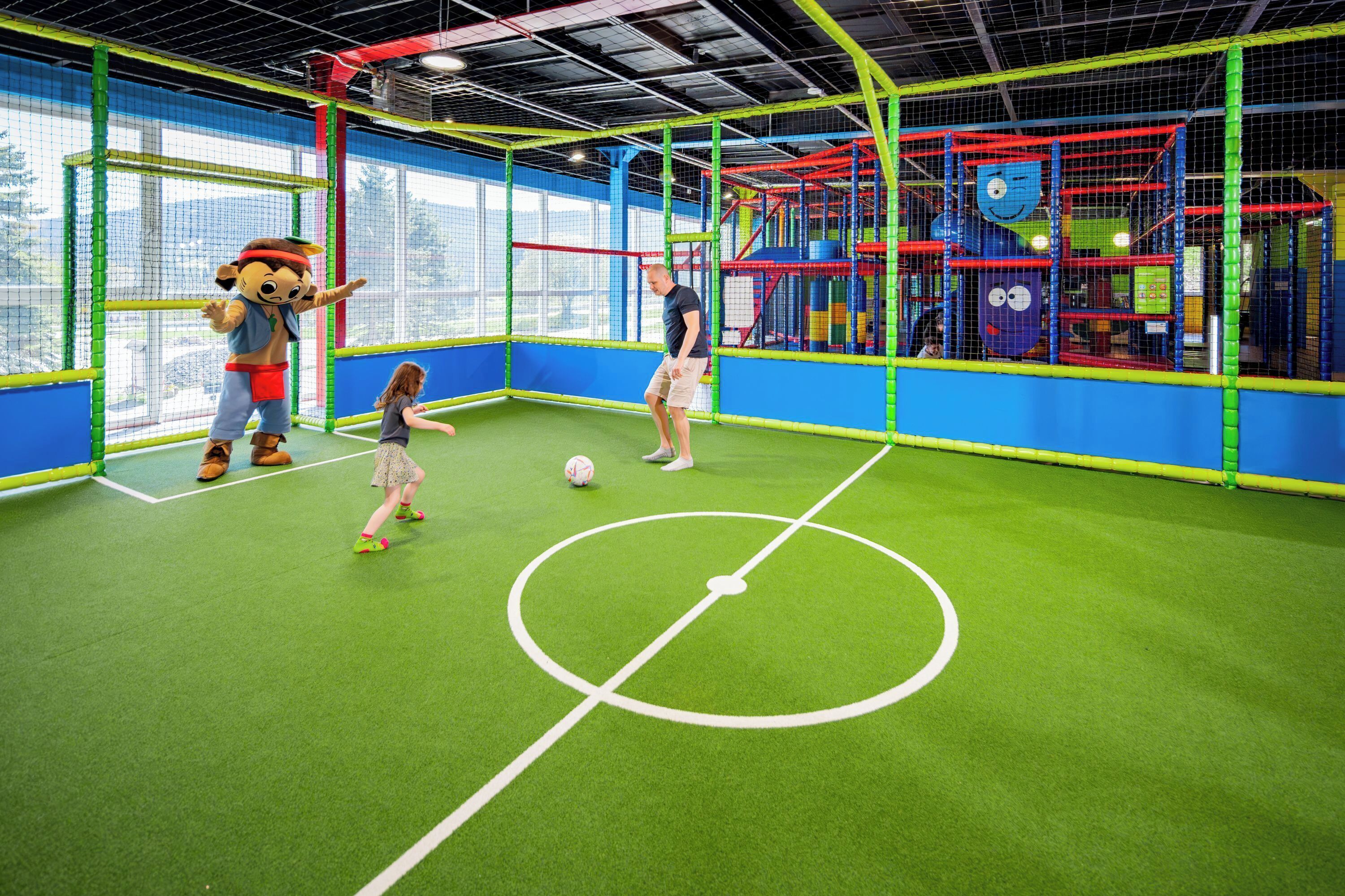 An indoor play area with a soccer field, netted play structures, and a mascot.