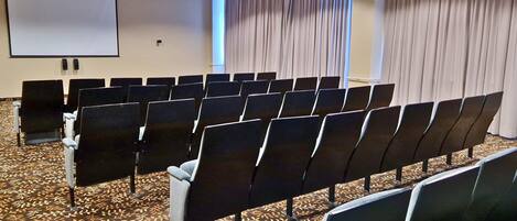 A conference room with rows of chairs, a projector screen, and curtains.