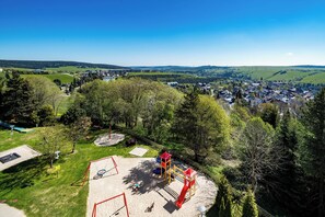 A playground with various play structures, surrounded by trees and a view of a town in the background.