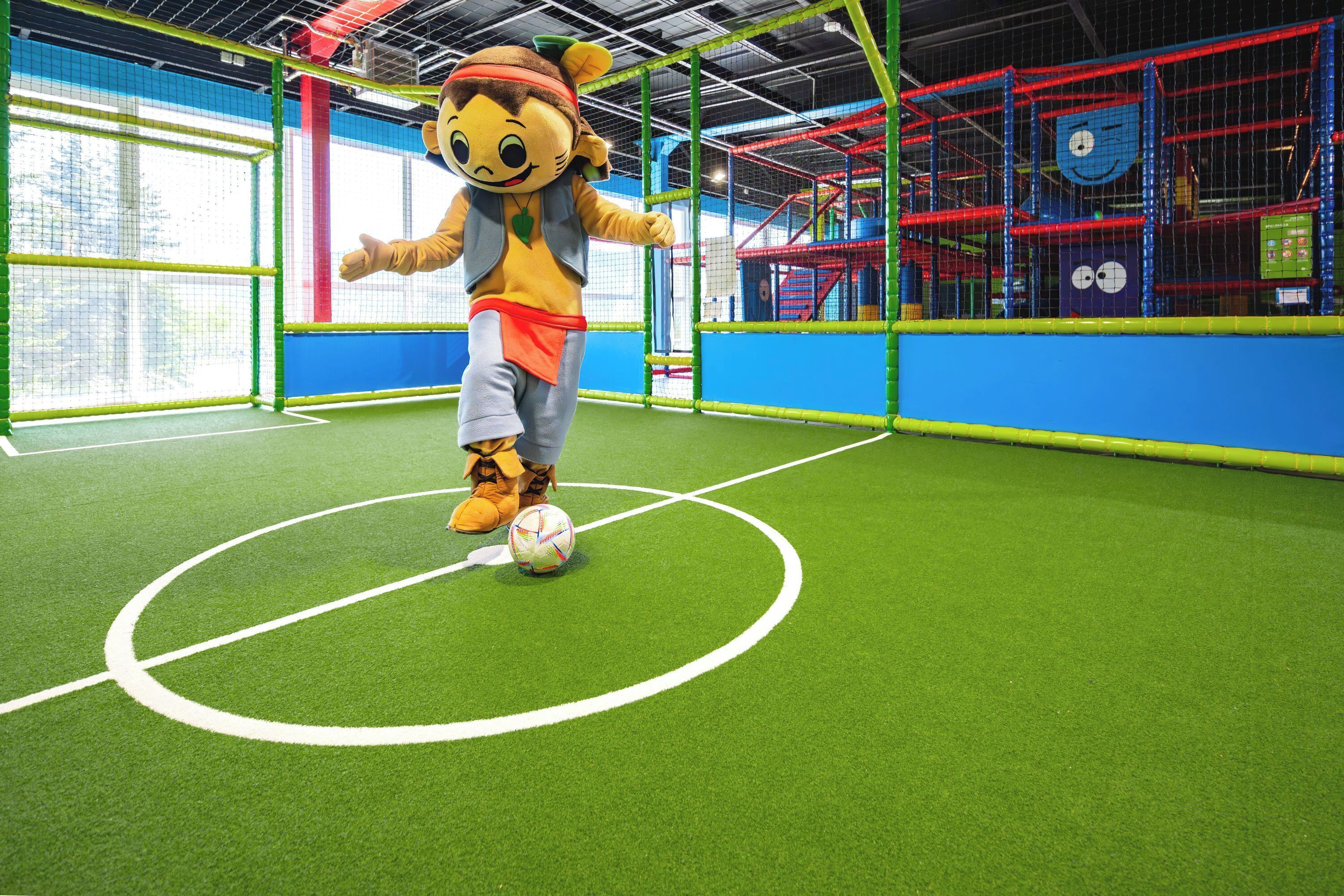 A mascot on a soccer field with safety netting and a blue wall in the background.