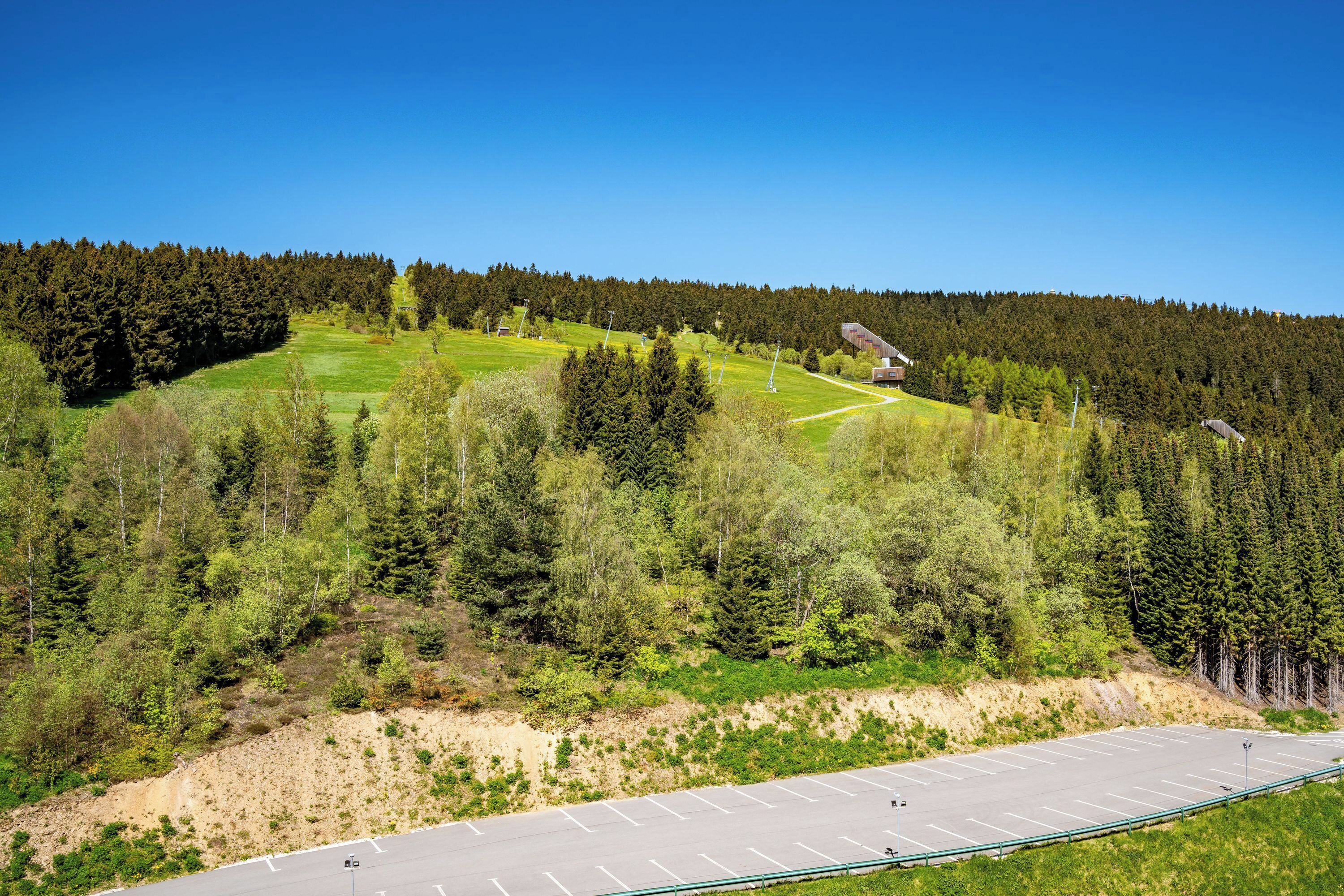 A parking lot with a clear view of a forested hillside and a building in the distance.