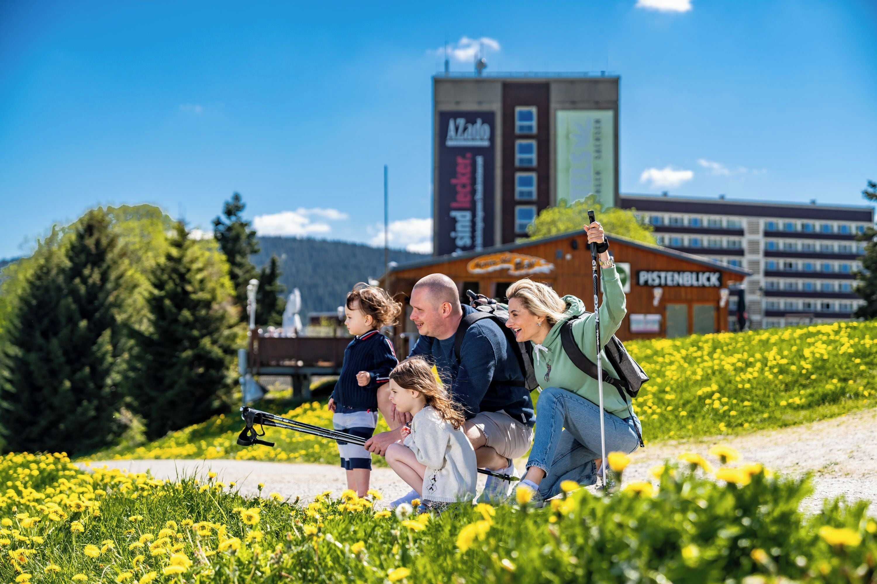 Eine Familie in einem Feld voller gelber Blumen, im Hintergrund ein Gebäude.