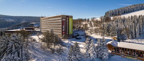 Un hotel de varios pisos, zona de estacionamiento y alrededores cubiertos de nieve.
