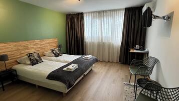 Habitación de hotel con cama de cabecera de madera, un escritorio con silla, una ventana con cortinas y una lámpara en el techo.