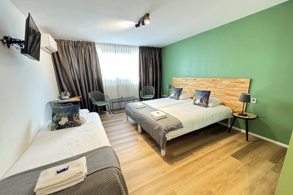 A hotel room with two beds, a TV mounted on the wall, a small table with chairs, and a green wall.