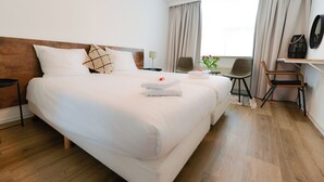 A hotel room with a large bed, two bedside tables, a chair, a desk, and a window with curtains. - Hotel de Grote Zwaan (De Lutte)