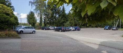 A parking lot with multiple cars parked, surrounded by trees and greenery.