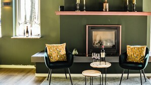 A cozy living room with two dark green armchairs, a small round table, and a fireplace. - Hotel de Grote Zwaan (De Lutte)