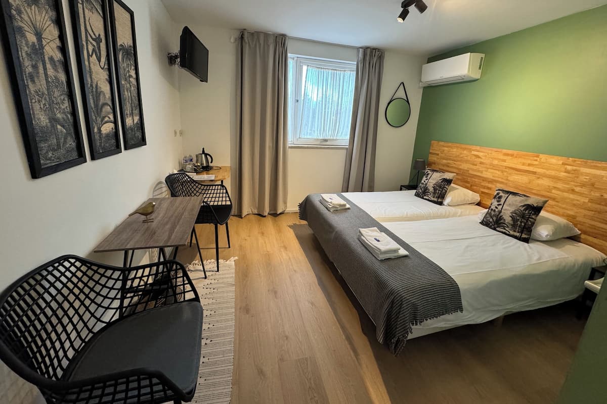 A hotel room with two beds, a desk, a chair, and a window with curtains.