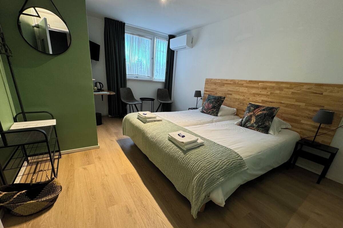 A hotel room with two beds, a desk, a chair, a mirror, and a window with curtains.