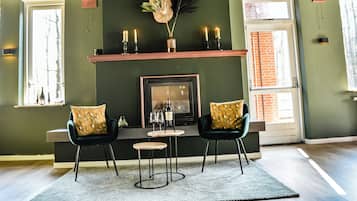 A room with a fireplace, two chairs, a small table, and a rug.
