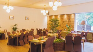 A dining area with multiple tables and chairs, a brick wall, and a large window with a view of greenery. - Hotel de Grote Zwaan (De Lutte)