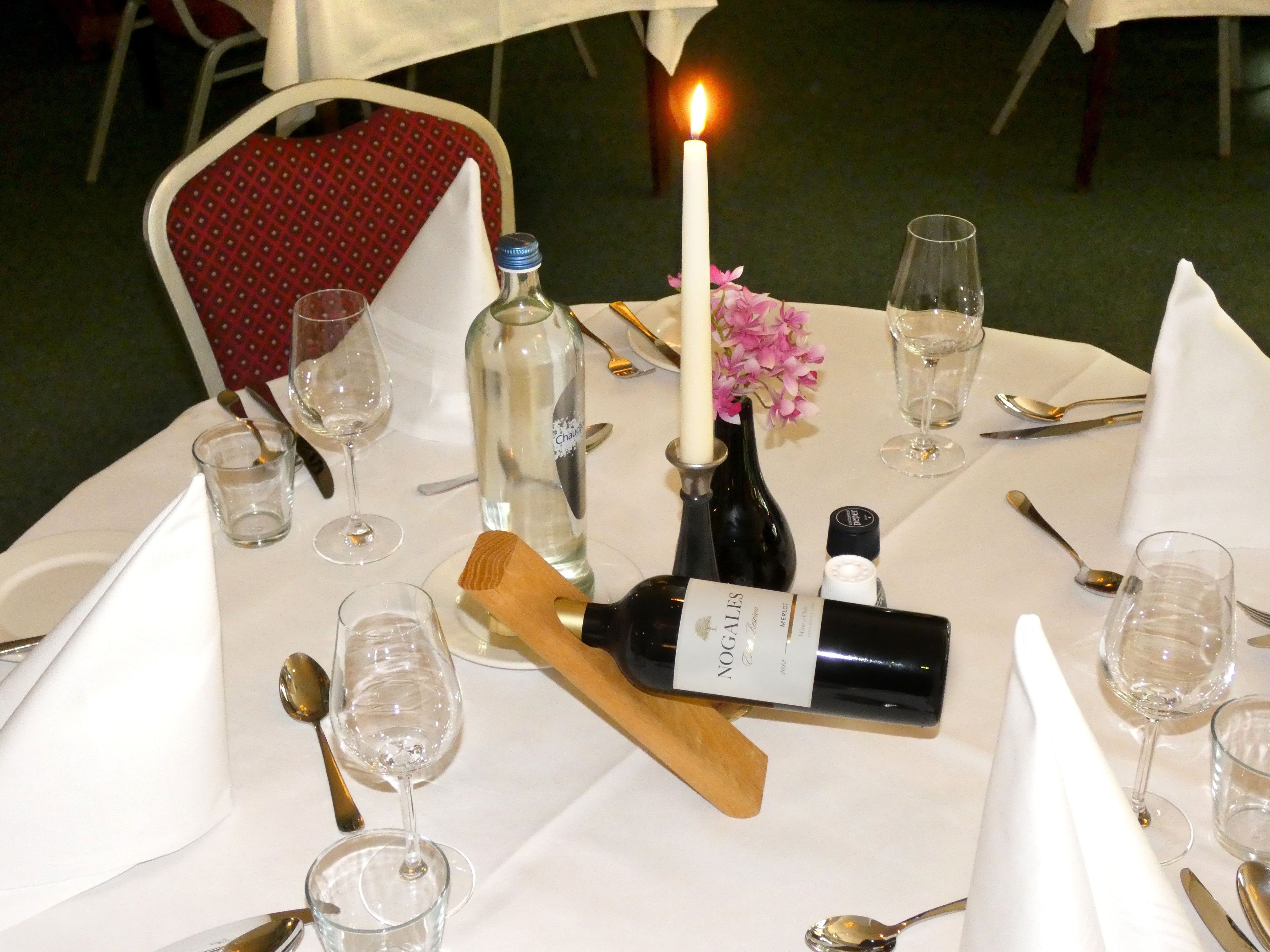 A table set for a meal with a candle, wine glasses, and a bottle of wine.