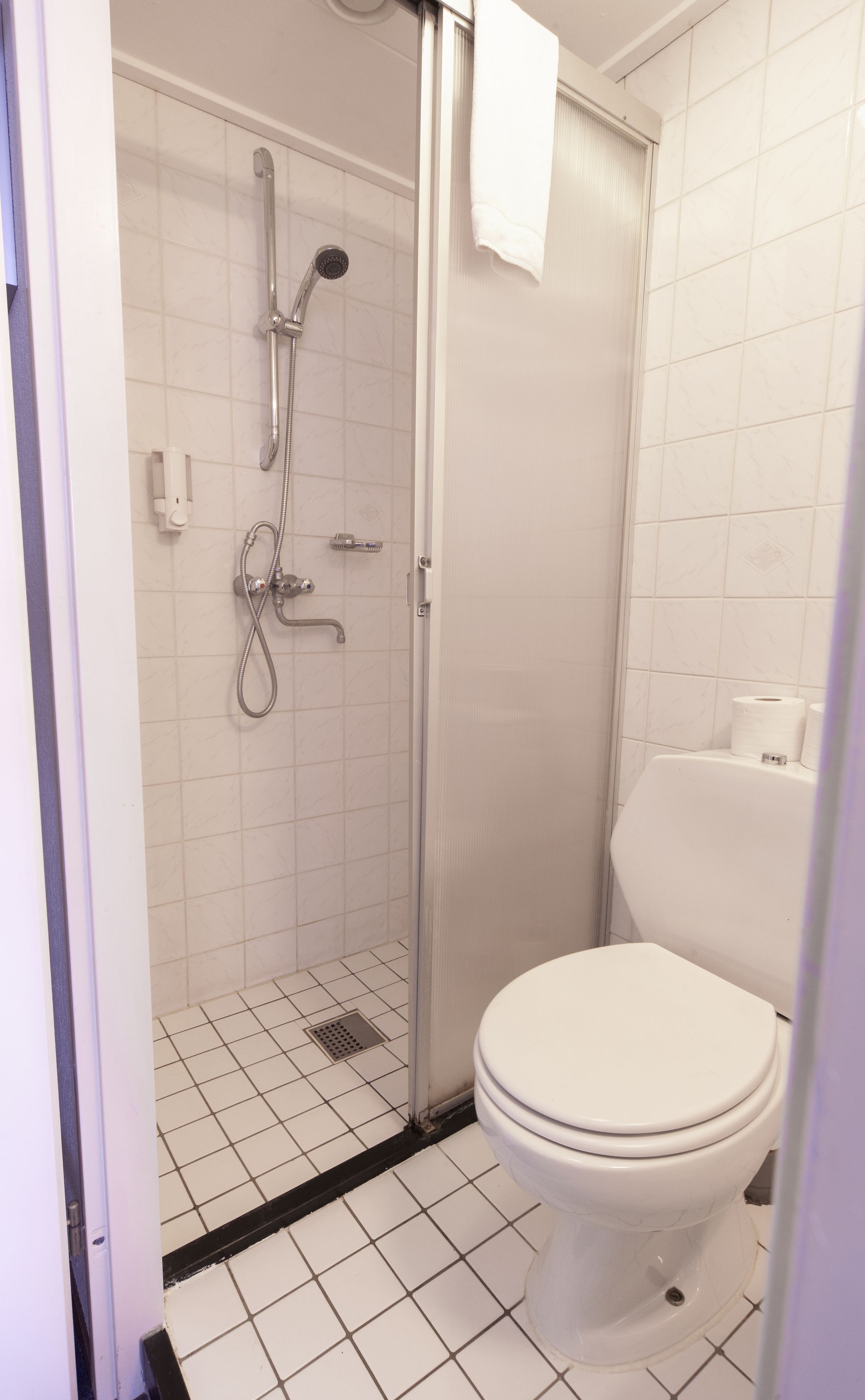 A bathroom with a white toilet, a shower with a glass door, and a tiled floor.