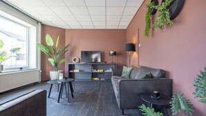 Ein modernes Wohnzimmer mit einer Couch, einem Fernseher, einem kleinen Tisch und einer Topfpflanze.