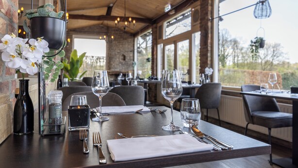 Ein Restaurant mit Holztisch, gedeckt für ein Essen, mit einer Vase weißer Orchideen, einer schwarzen Kerze und Weingläsern.