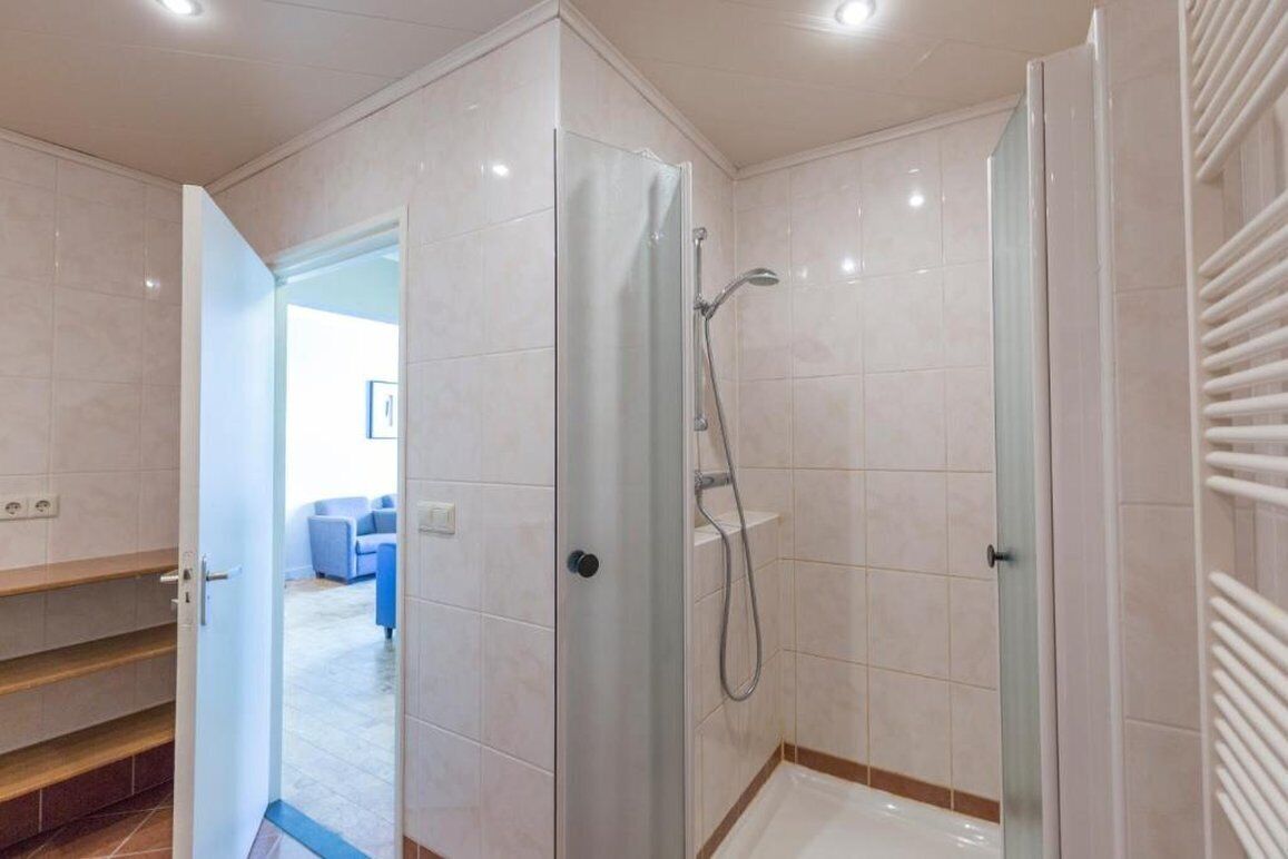 Un baño moderno con ducha envuelta en vidrio, piso de baldosas blancas y una escalera visible que conduce a otra área.
