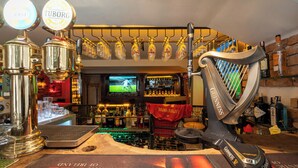 Een bar met een harp, meerdere bierkraan tappunten waaronder Tuborg en Guinness, en een televisie op de achtergrond.