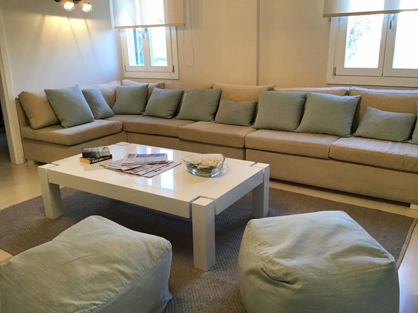 A living room with a beige sectional sofa, a white coffee table, and two light green poufs.