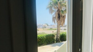 A balcony with a white chair, a palm tree, and a view of buildings in the distance. - Thera Mare (Santorini)