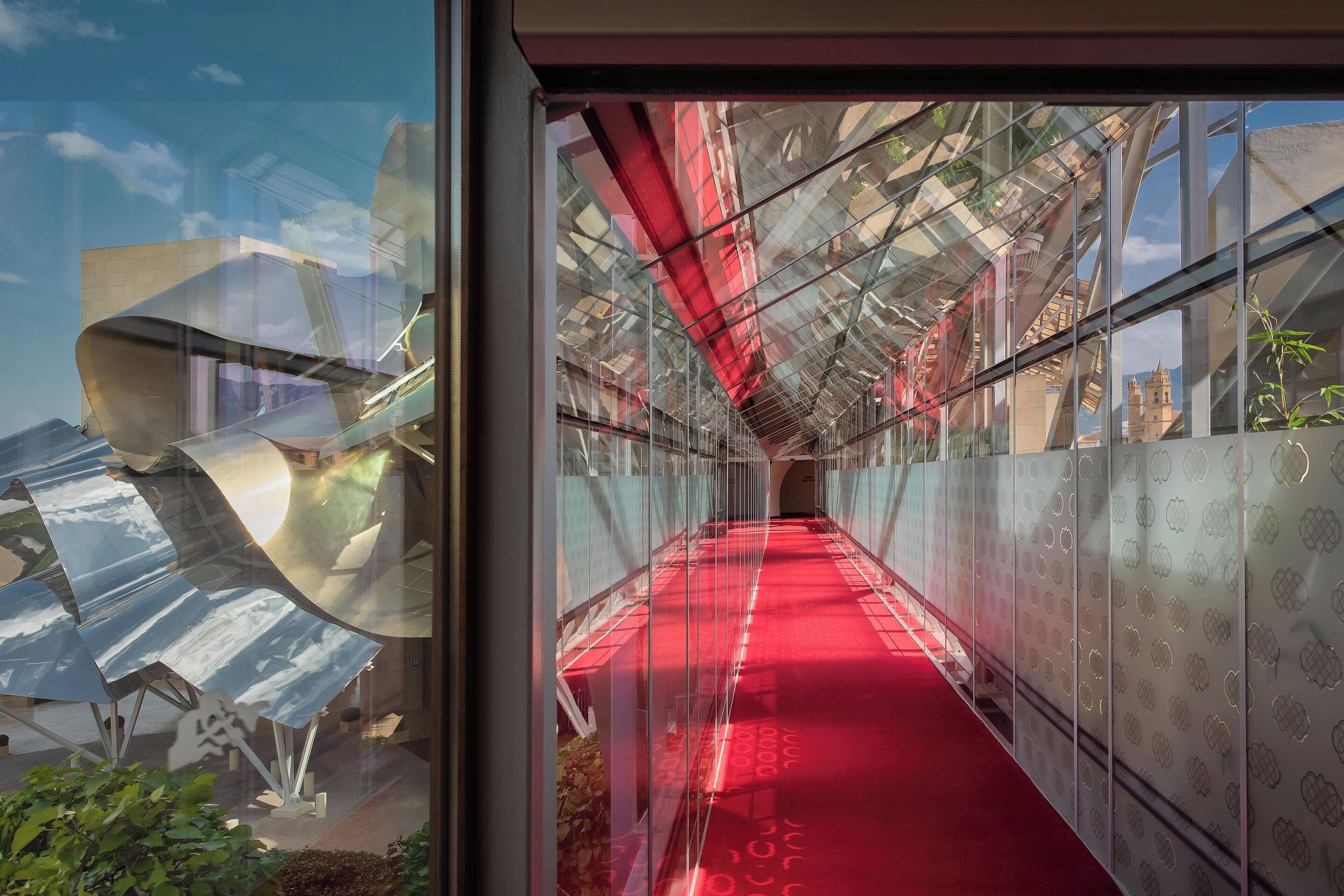 A corridor with a red carpet, glass walls, and a metal structure.