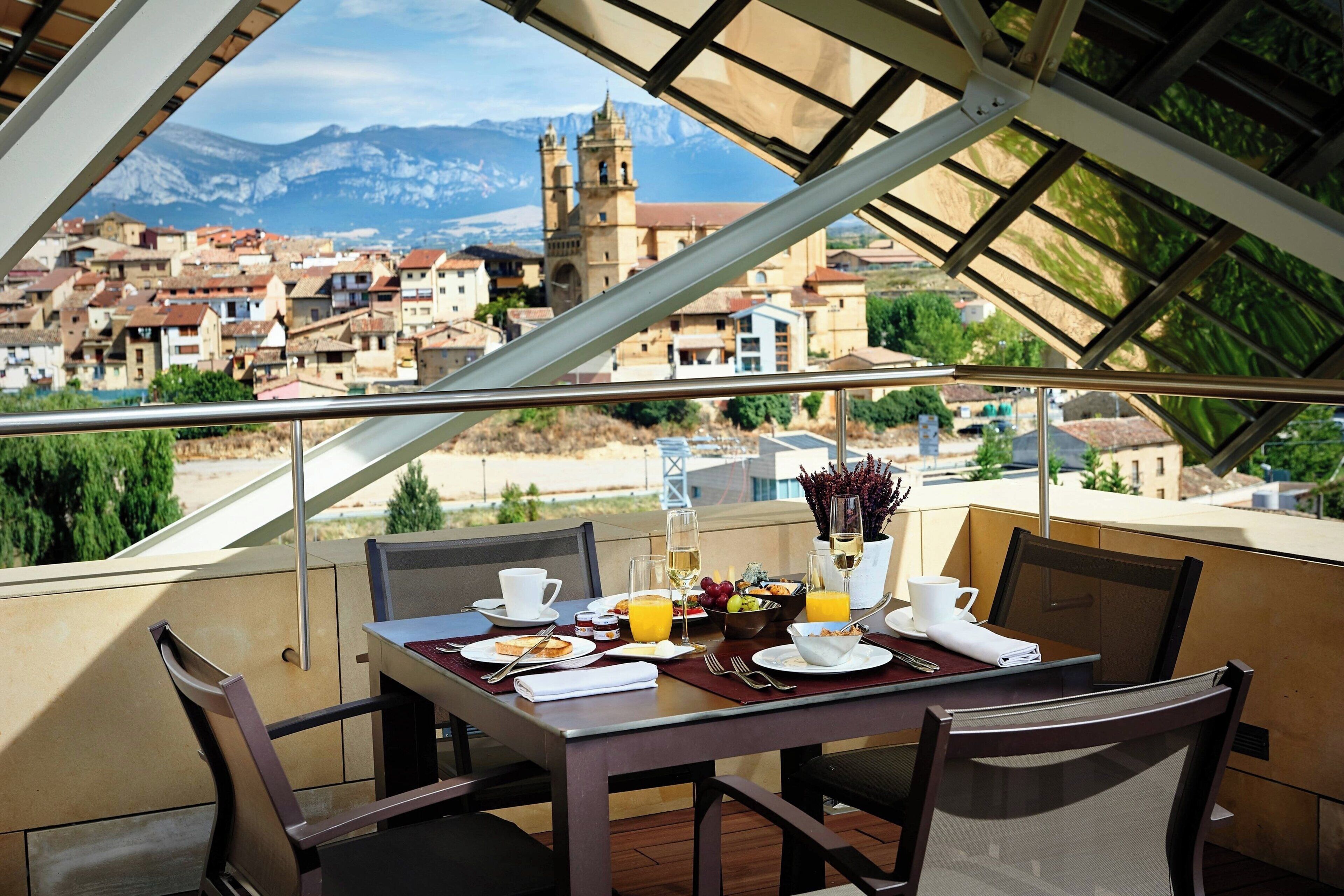 A dining table set with breakfast items, a view of a town with a church, and mountains in the background.