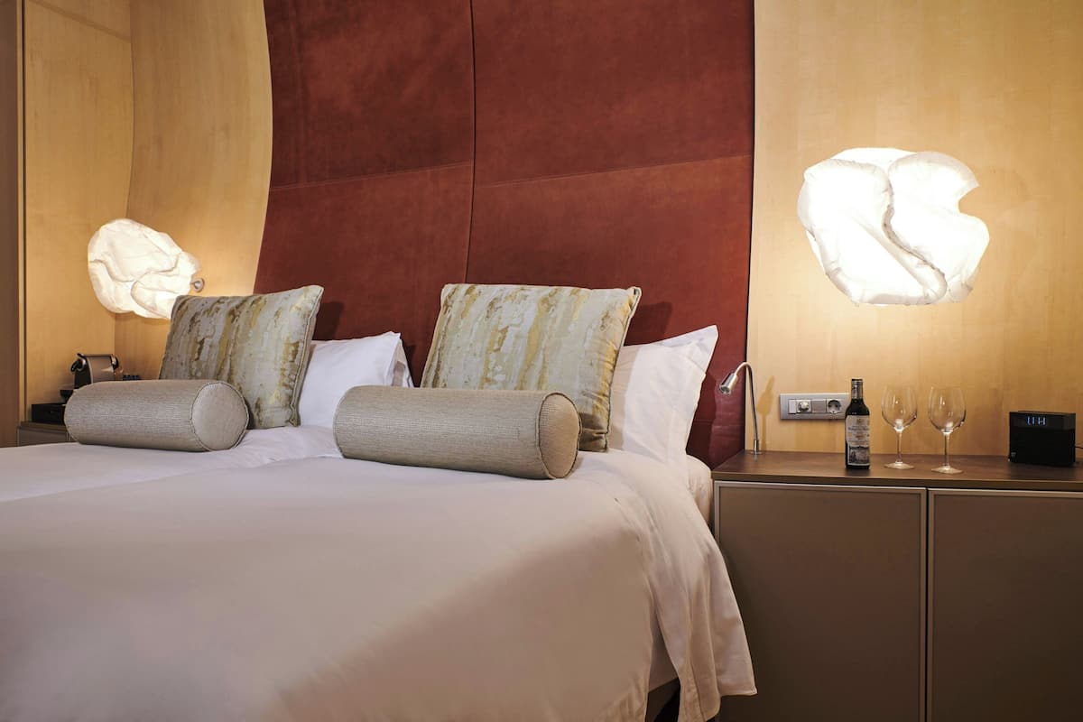 A neatly made bed with pillows and a nightstand with a bottle and glasses.