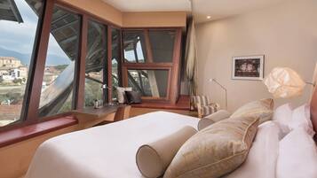 A hotel room with a large bed, multiple windows, a bedside table, a lamp, and a framed picture on the wall.