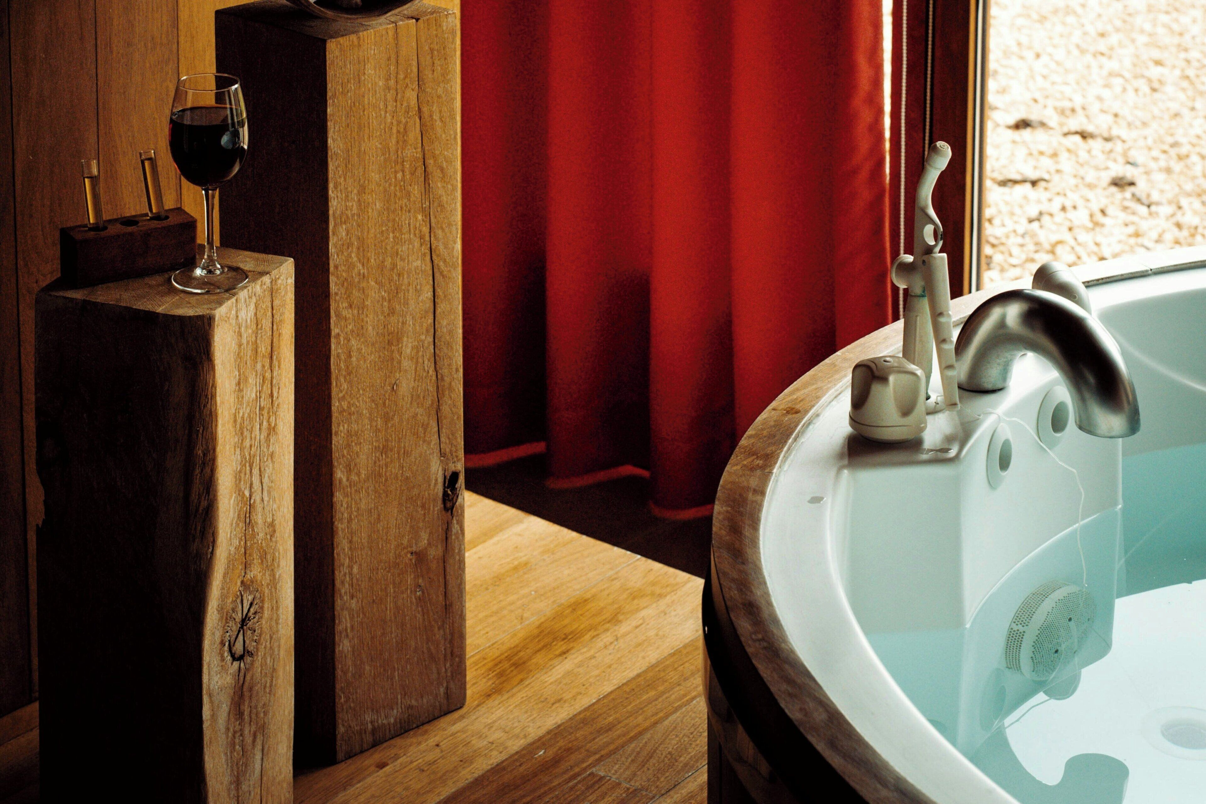 Eine Holzwanne mit Wasserhahn, ein Glas Rotwein und ein roter Vorhang im Hintergrund.