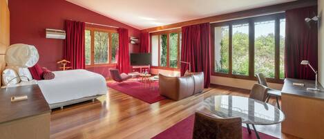 A modern hotel room with a large bed, a desk, a TV, and a dining area.