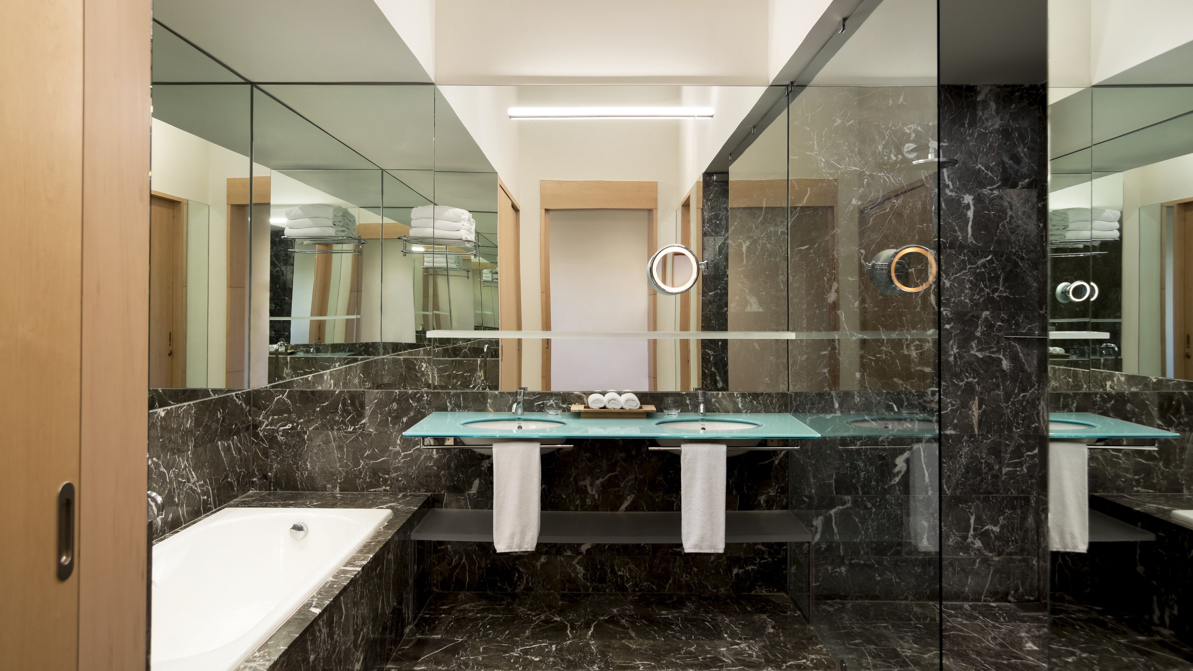 A modern bathroom with a glass-enclosed shower, a white bathtub, and a marble-tiled vanity with two sinks.