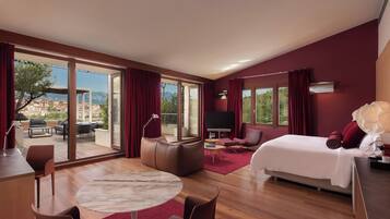 A modern hotel room with a large sliding glass door leading to an outdoor terrace, a king-sized bed, a seating area with a TV, and a dining table.