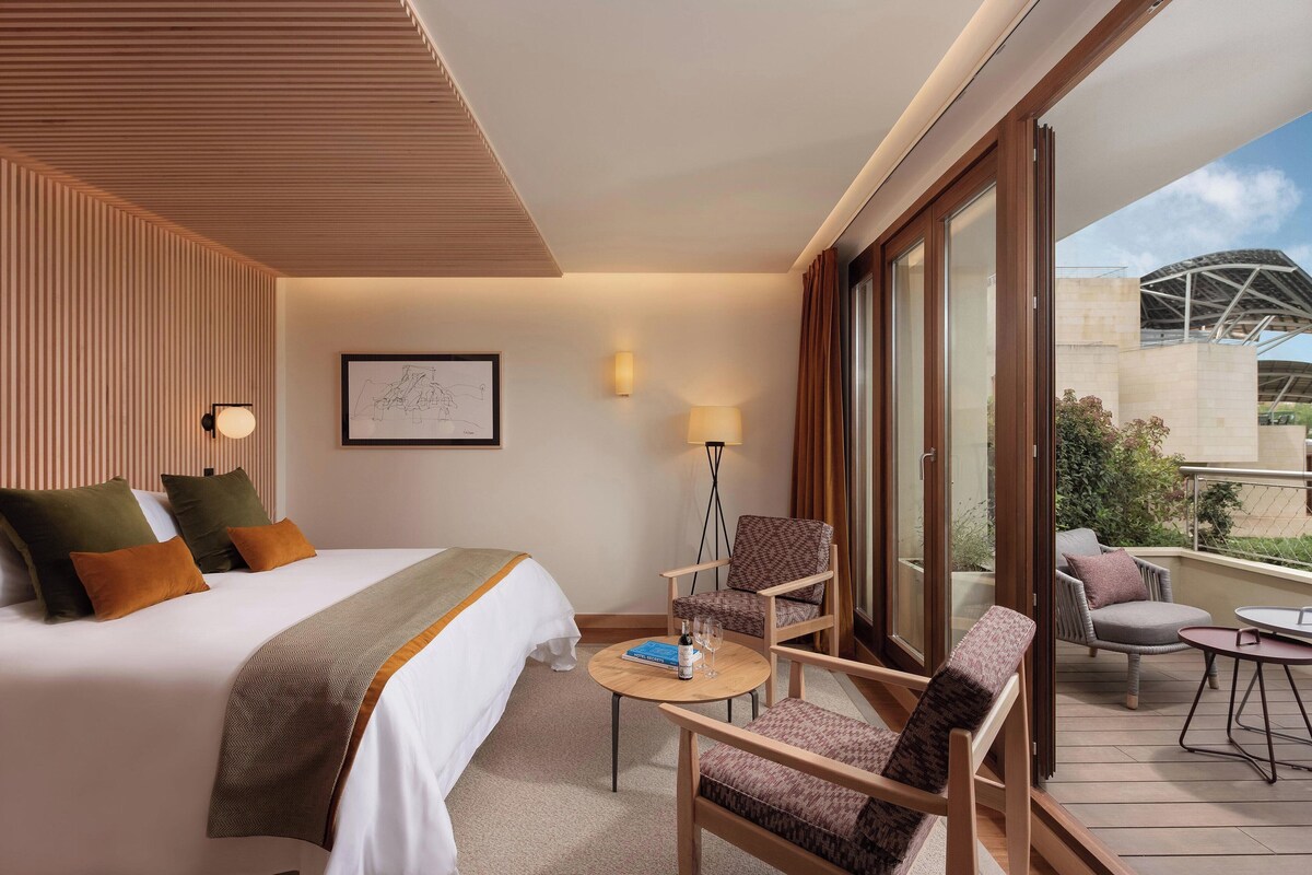 Une chambre d’hôtel équipée d’un lit, d’un bureau, d’une chaise et d’un balcon donnant sur un immeuble.